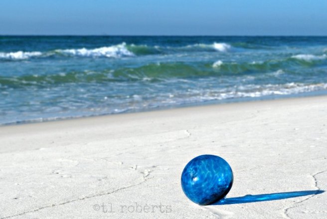blue glass Christmas ornament on a white, sand beach