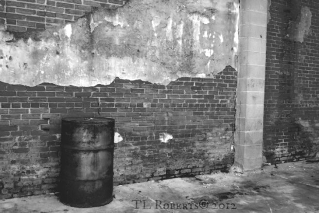 black and white shot of a metal trashcan against a brick wall